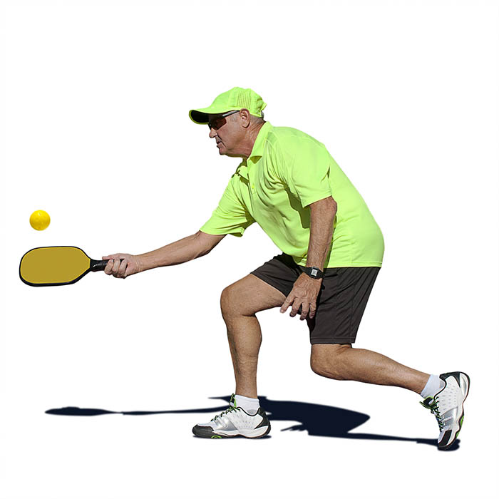 senior man hitting a forehand stroke during pickleball match.